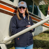 Woman wearing Flight Outfitters Women's Airfoil Insulated Jacket with hat in front of Cessna high-wing aircraft"