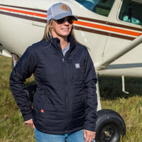 Woman wearing Flight Outfitters Women's Airfoil Insulated Jacket with hat in front of Cessna 172 aircraft