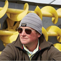 Flight Outfitters owner Mark Glassmeyer wearing grey with black stripe beanie in front of farm equipment