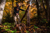 A man cutting a tree in the forest while wearing the Flight Outfitters Retro Logo Long Sleeve T-Shirt, emphasizing its rugged versatility.