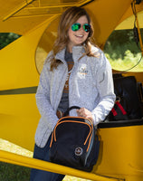 A woman wearing the Women's Fairbanks Fleece in Heather Stone, standing in front of an aircraft, showcasing its aviation-inspired versatility.