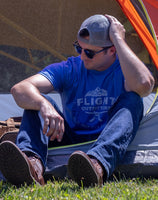 A man sitting in front of a tent wearing the Flight Outfitters Mountain Range T-Shirt, emphasizing its adventure-ready style.