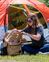 A woman opening the Flight Outfitters Bush Pilot Rucksack, showing easy access to its compartments.